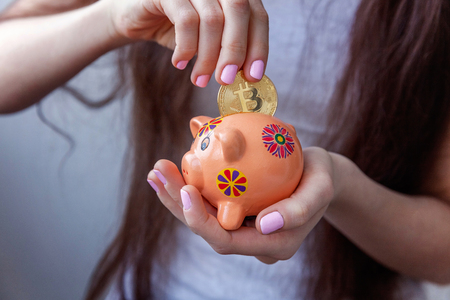 Piggy bank, woman hand holds golden bitcoin coin virtual money. Cryptocurrency and saving conceptの写真素材