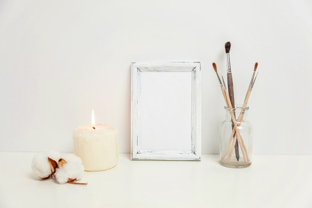 Vertical frame mockup with candle brush vase near white wall. Empty frame mock up for presentation design. Template framing for modern art. Hygge scandinavian style workspace. Natural eco home decorの写真素材