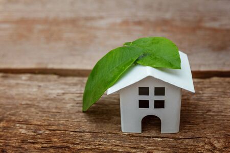 Miniature white toy model house with green leaves on wooden backgdrop. Eco Village, abstract environmental background. Real estate mortgage property insurance dream home ecology conceptの写真素材