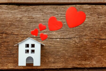 Miniature white toy house with red hearts on a rustic old vintage wooden background. Mortgage property insurance dream home conceptの写真素材