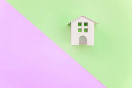 Miniature white toy house on violet and green pastel color paper geometric flat lay background. Mortgage property insurance dream home concept. Copy space for advertisementの写真素材
