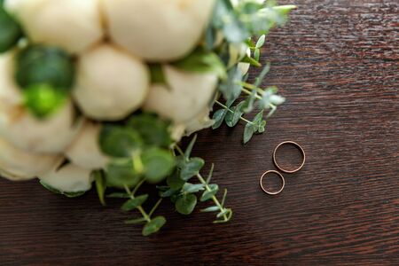 Beautiful wedding rings lie on wooden surface against background of bouquet of flowers. Declaration...