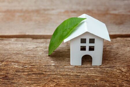 Miniature white toy model house with green leaves on wooden backgdrop. Eco Village, abstract environmental background. Real estate mortgage property insurance dream home ecology conceptの写真素材