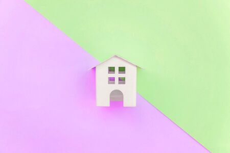 Miniature white toy house on violet and green pastel color paper geometric flat lay background. Mortgage property insurance dream home concept. Copy space for advertisementの写真素材