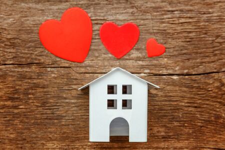 Miniature white toy house with red hearts on a rustic old vintage wooden background. Mortgage property insurance dream home conceptの写真素材