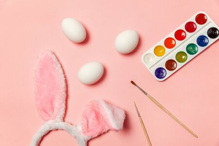 Happy Easter concept. Preparation for holiday. Decorative eggs colorful paints and bunny ears furry costume isolated on trendy pastel pink background. Simple minimalism flat lay top view copy spaceの写真素材