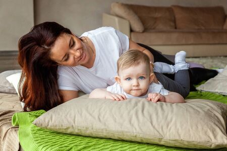 Young mother playing with her young daughter. Woman and new born girl relax in a bedroom. Mother...