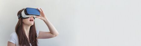 Smile young woman wearing using virtual reality VR glasses helmet headset on white background. Smartphone using with virtual reality goggles. Technology, simulation, hi-tech, videogame concept. Bannerの写真素材