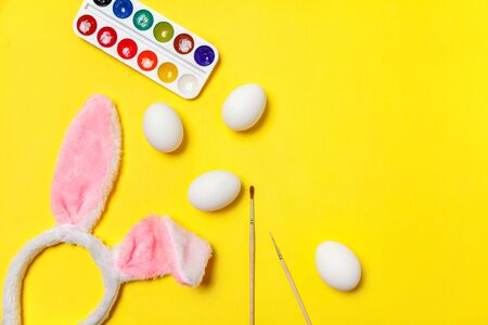 Happy Easter concept. Preparation for holiday. Decorative eggs colorful paints and bunny ears furry costume toy isolated on trendy yellow background. Simple minimalism flat lay top view copy spaceの写真素材