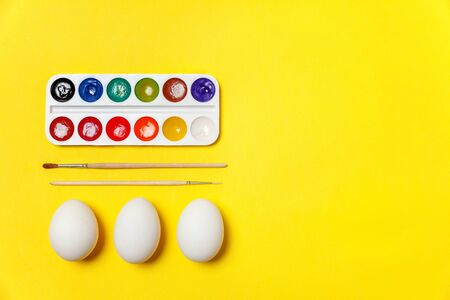 Happy Easter concept. Preparation for holiday. Decorative eggs colorful paints and brushes isolated on trendy yellow background. Simple minimalism flat lay top view copy spaceの写真素材