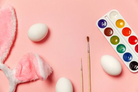 Happy Easter concept. Preparation for holiday. Decorative eggs colorful paints and bunny ears furry costume isolated on trendy pastel pink background. Simple minimalism flat lay top view copy spaceの写真素材