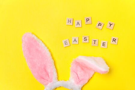 Happy Easter concept. Preparation for holiday. Inscription HAPPY EASTER letters decorative bunny ears isolated on trendy yellow background. Simple minimalism flat lay top view copy spaceの写真素材