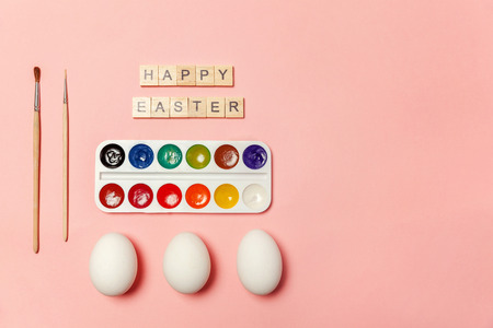 Happy Easter concept. Preparation for holiday. Inscription HAPPY EASTER letters eggs colorful paints isolated on trendy pastel pink background. Simple minimalism flat lay top view copy spaceの写真素材
