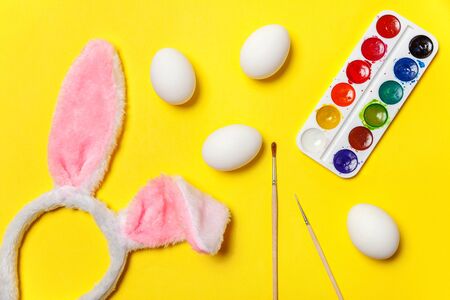 Happy Easter concept. Preparation for holiday. Decorative eggs colorful paints and bunny ears furry costume toy isolated on trendy yellow background. Simple minimalism flat lay top view copy spaceの写真素材