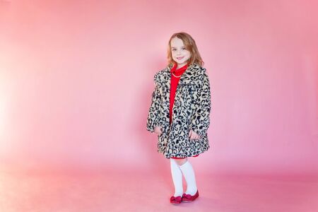 Little cute sweet smiling girl in red dress standing on pink colourful pastel trendy modern fashion...