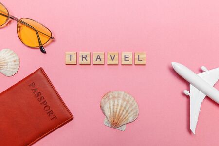 Vacation travel summer weekend adventure trip concept. Minimal simple flat lay with Inscription TRAVEL letters plane passport sunglasses and shell on pink pastel trendy background. Tourist essentialsの写真素材