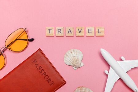 Vacation travel summer weekend adventure trip concept. Minimal simple flat lay with Inscription TRAVEL letters plane passport sunglasses and shell on pink pastel trendy background. Tourist essentialsの写真素材