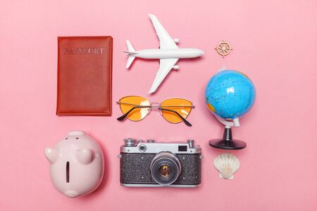Vacation travel summer weekend sea adventure trip concept. Minimal simple flat lay with plane vintage camera passport sunglasses globe piggy bank and shell on pink pastel trendy modern backgroundの写真素材
