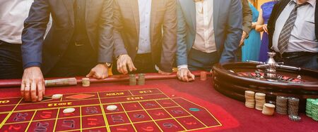 Group of people behind roulette gambling table in luxury casino. Friends playing poker at roulette...