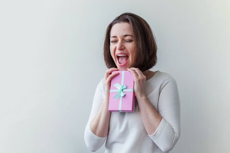 Young positive woman holding small pink gift box isolated on white background. Preparation for...