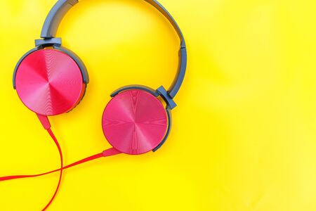 Red headphones on yellow background. Minimalist simple photo of earphones with copy space. Red dj headphones with cable isolated on colorful backdrop, flat lay top view. Music conceptの写真素材