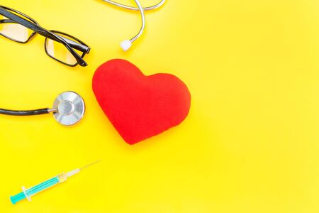Simply minimal design medicine equipment stethoscope or phonendoscope glasses syringe red heart isolated on trendy yellow background. Instrument device for doctor. Health care life insurance conceptの写真素材