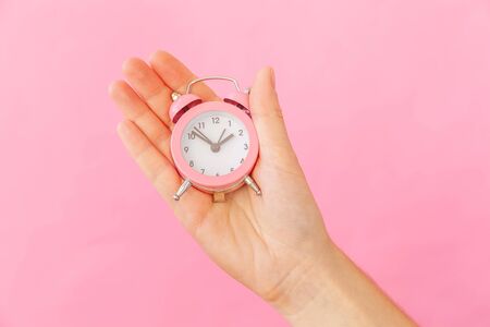 Simply design female woman hand holding ringing twin bell alarm clock isolated on pink pastel colorful trendy background. Rest hours time of life good morning night wake up awake concept. Copy spaceの写真素材