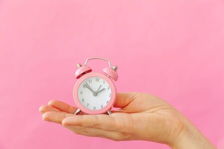 Simply design female woman hand holding ringing twin bell alarm clock isolated on pink pastel...