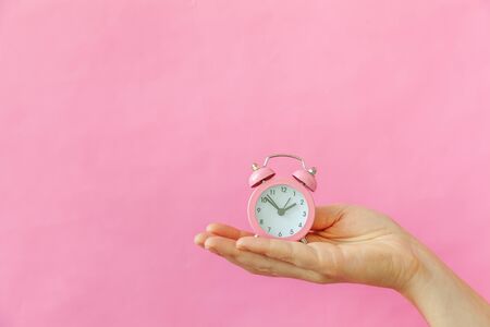 Simply design female woman hand holding ringing twin bell alarm clock isolated on pink pastel colorful trendy background. Rest hours time of life good morning night wake up awake concept. Copy spaceの写真素材