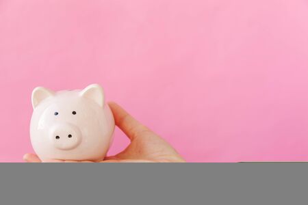 Simply design female woman hand holding piggy bank isolated on pink pastel colorful trendy background. Saving investment budget business wealth retirement financial money banking concept. Copy spaceの写真素材