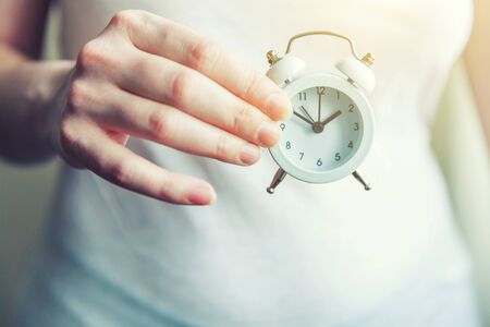 Female woman hands holding ringing twin bell vintage classic alarm clock. Rest hours time of life good morning night wake up awake conceptの写真素材