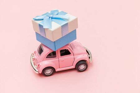 Simply design pink vintage retro toy car delivering gift box on roof isolated on trendy pastel pink background. Christmas New Year birthday Valentine's day celebration present romantic concept.の写真素材