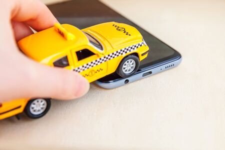 Smartphone application of taxi service for online searching calling and booking cab concept. Hand holding yellow toy car Taxi Cab on empty screen of smart phone on wooden background. Taxi symbolの写真素材