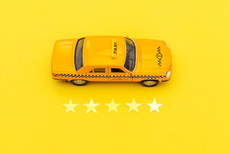 Yellow toy car Taxi Cab and 5 stars rating isolated on yellow background. Smartphone application of taxi service for online searching calling and booking cab concept. Taxi symbol. Copy spaceの写真素材