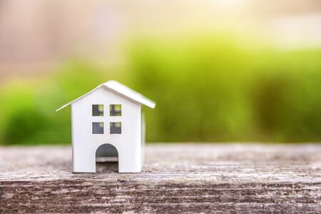 Miniature white toy model house in wooden background near green backdrop. Eco Village, abstract environmental background. Real estate mortgage property insurance dream home ecology conceptの写真素材