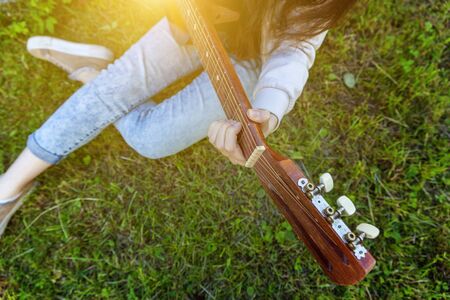Closeup of woman hands playing acoustic guitar on park or garden background. Teen girl learning to...