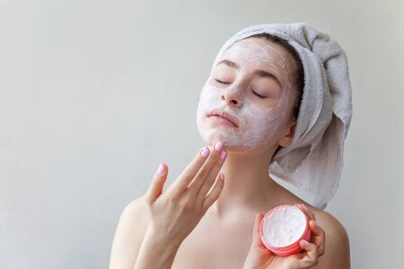 Beauty portrait of woman in towel on head with white nourishing mask or creme on face, white background isolated. Skincare cleansing eco organic cosmetic spa relax conceptの写真素材
