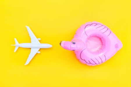 Summer beach composition. Minimal simple flat lay with plane and Inflatable flamingo isolated on yellow background. Vacation travel adventure trip concept. Top view copy spaceの写真素材