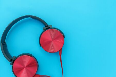Red headphones on turquoise blue background. Minimalist simple photo of earphones with copy space. Red dj headphones with cable isolated on pastel colorful backdrop, flat lay top view. Music conceptの写真素材