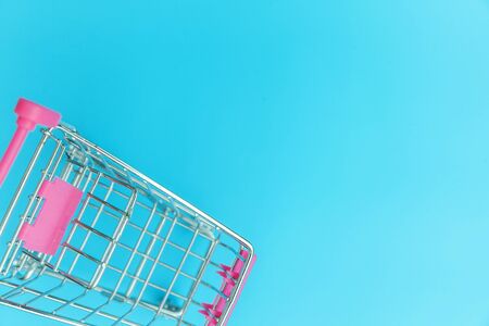 Small supermarket grocery push cart for shopping toy with wheels isolated on blue pastel colorful trendy background Copy space. Sale buy mall market shop consumer conceptの写真素材