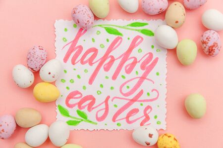 Happy Easter concept. Inscription HAPPY EASTER letters candy chocolate eggs and jellybean sweets isolated on trendy pastel pink background. Simple minimalism flat lay top view copy spaceの写真素材