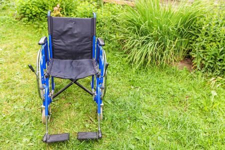 Empty wheelchair standing on grass in hospital park waiting for patient services. Invalid chair for disabled people parked outdoor in nature. Handicap accessible symbol. Health care medical conceptの写真素材
