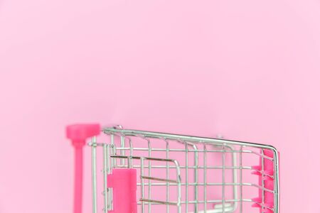 Small supermarket grocery push cart for shopping toy with wheels isolated on pink pastel colorful trendy background. Sale buy mall market shop consumer concept. Copy spaceの写真素材