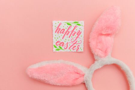 Happy Easter concept. Preparation for holiday. Inscription HAPPY EASTER letters decorative bunny ears isolated on trendy pastel pink background. Simple minimalism flat lay top view copy spaceの写真素材