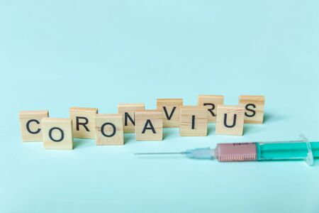Text phrase Coronavirus and syringe on blue pastel background.