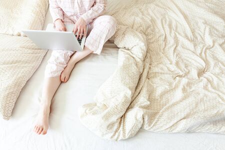 Young woman in pajamas sitting on bed at home working using on laptop pc computer.の写真素材