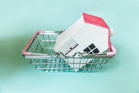 Simply design with miniature white toy house and supermarket grocery shopping basket isolated on blue background. Mortgage property insurance dream home concept. Copy spaceの写真素材