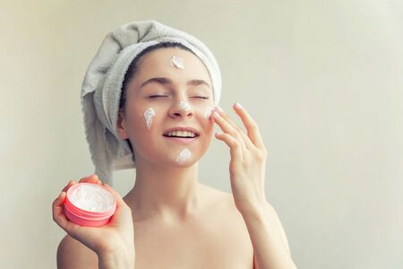 Beauty portrait of woman in towel on head with white nourishing mask or creme on face, white background isolated. Skincare cleansing eco organic cosmetic spa relax conceptの写真素材