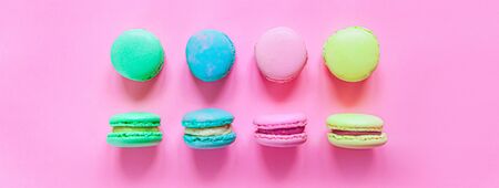 Sweet almond colorful pink blue yellow green macaron or macaroon dessert cake isolated on trendy pink pastel background. French sweet cookie. Minimal food bakery concept. Flat lay top view bannerの写真素材