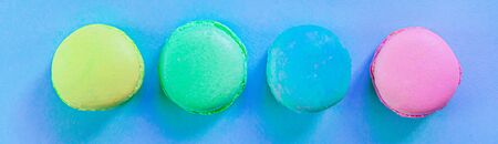 Sweet almond colorful pink blue yellow green macaron or macaroon dessert cake isolated on trendy blue pastel background. French sweet cookie. Minimal food bakery concept. Flat lay copy space bannerの写真素材